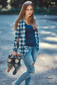 Portrait of a beautiful girl with long hair wearing fleece shirt and jeans, holds rollers, standing in a countryside.